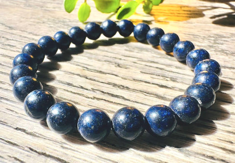 Blue beaded bracelet on a wooden surface with green leaves in the background