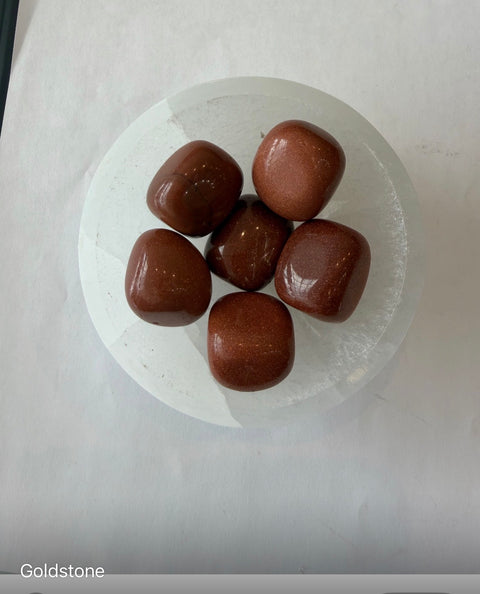 Goldstone Tumbled Stones in selenite bowl — sparkling crystals for ambition, confidence, and goal setting.