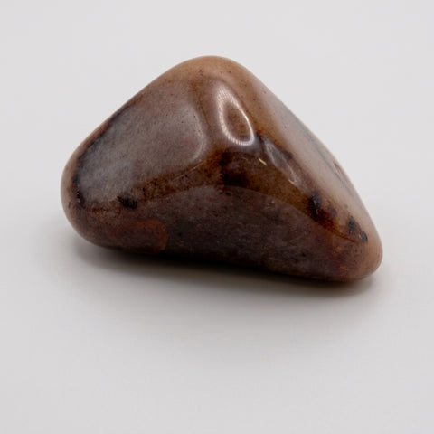 Single polished red aventurine tumbled stone in muted reddish-brown on a studio background