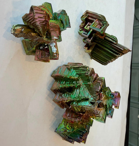 Three rainbow bismuth crystals shown together displaying natural variation in shape and color