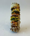 White sage smudge stick wrapped in white string and decorated with vibrant yellow, orange, and green dried flowers, on a white background.